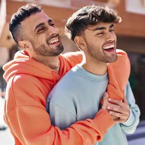 Two smiling men in colorful sweaters share a warm hug, representing unity and resilience against LGBTQ+ discrimination - Working For Workers