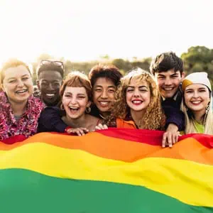 A diverse group of young individuals proudly holding a rainbow flag, symbolizing support for LGBTQ+ rights and workplace protections. -  Working For Workers